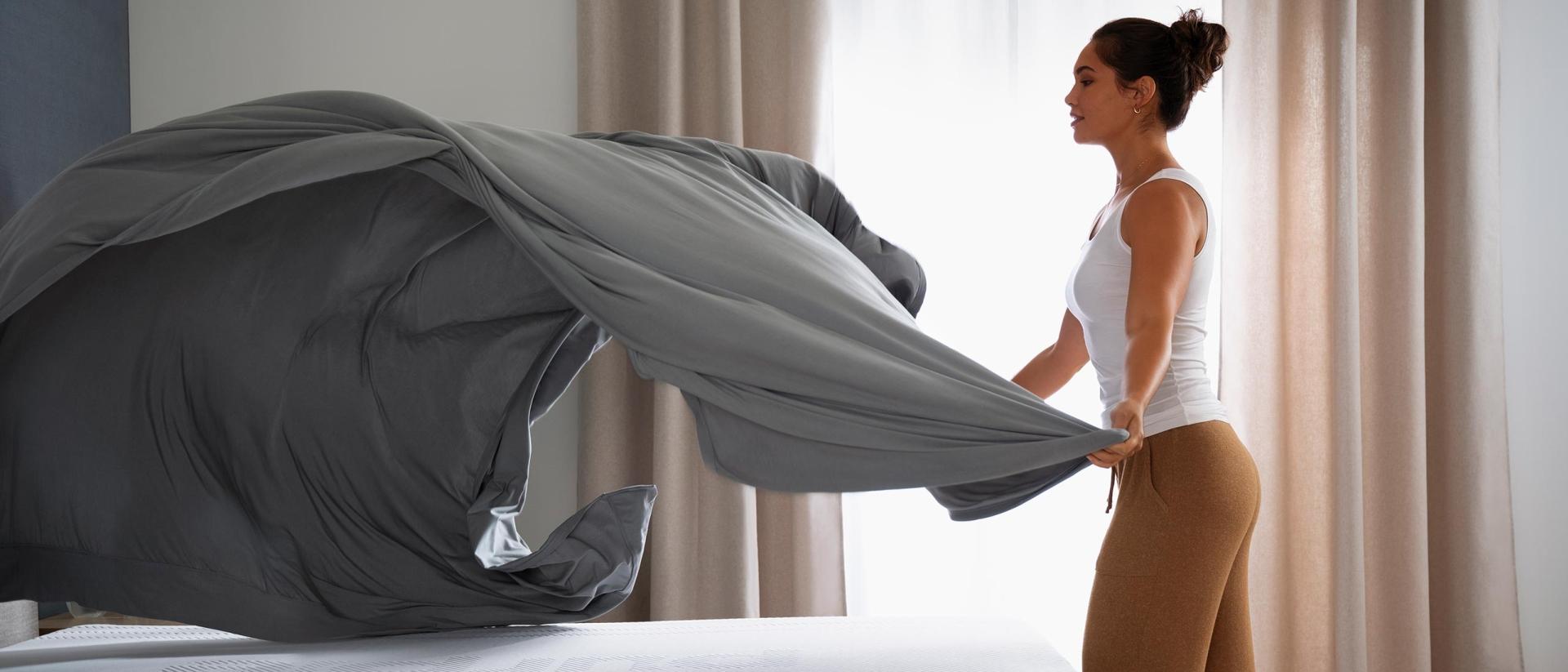 Woman placing a top sheet on a bed.