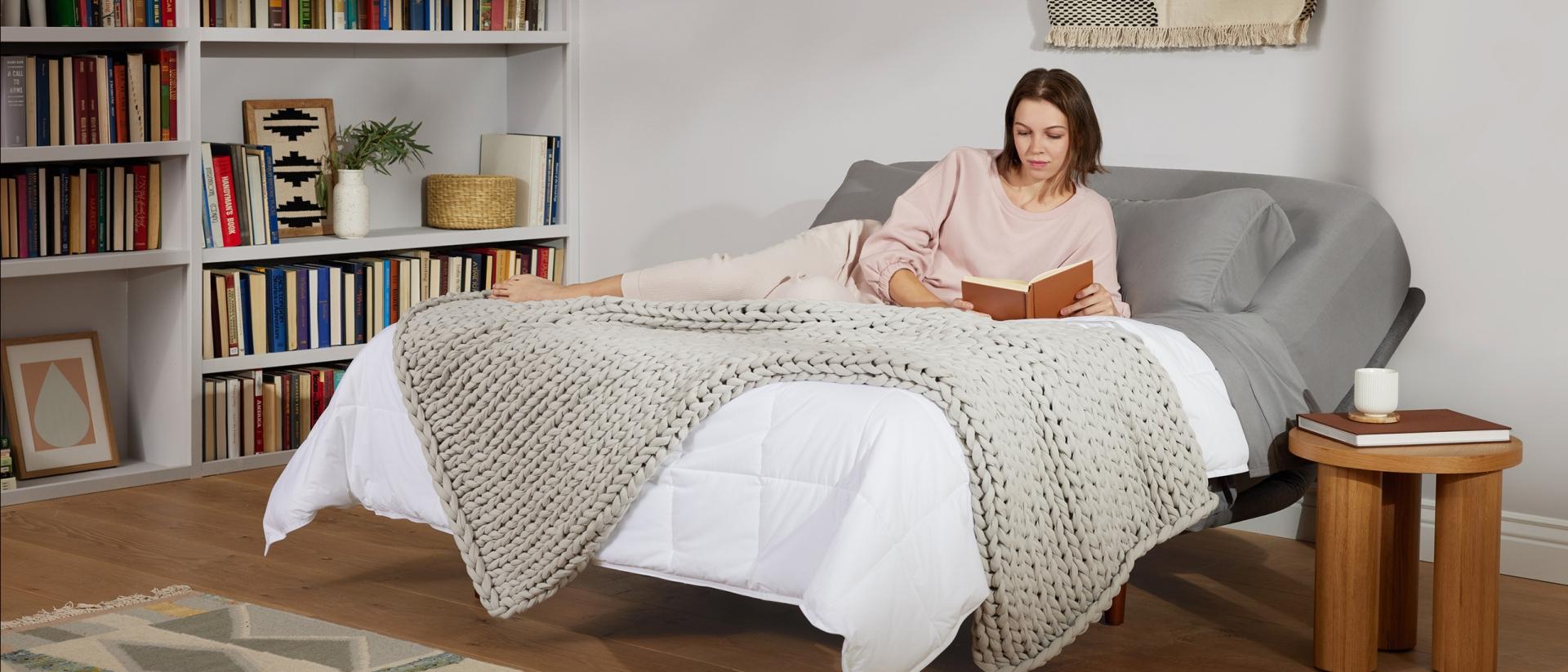 A woman reading a book while relaxing on an adjustable bed. 