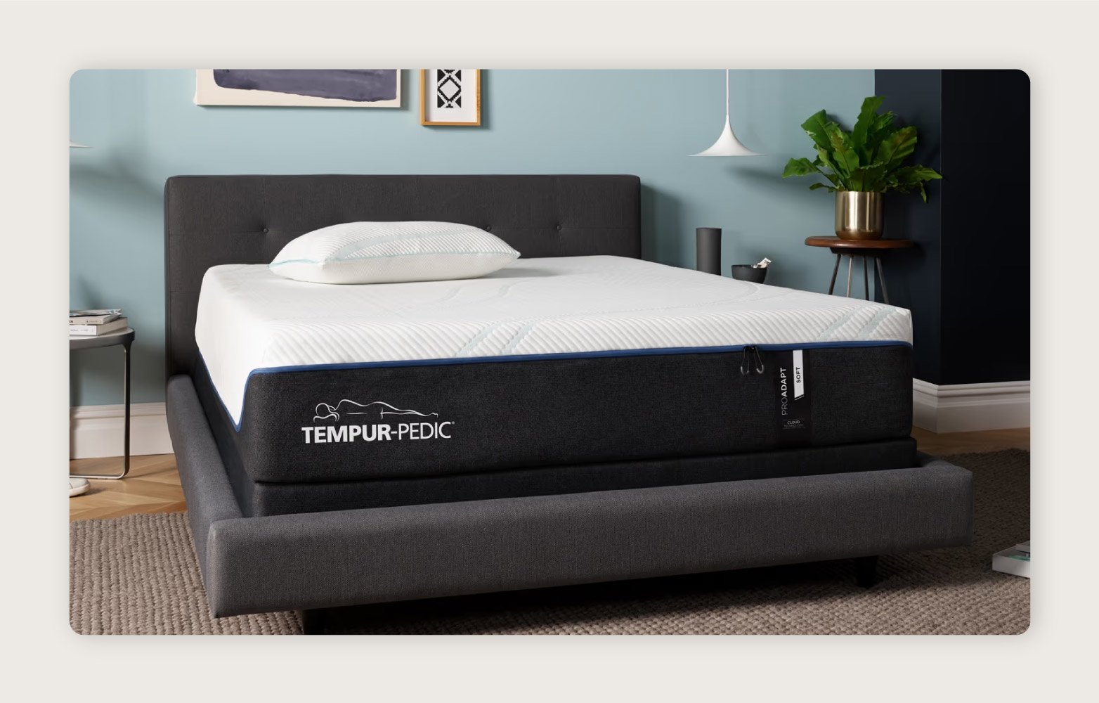  The TEMPUR-Adapt® ProAdapt Mattress on a charcoal gray upholstered bed frame in a light blue room. 