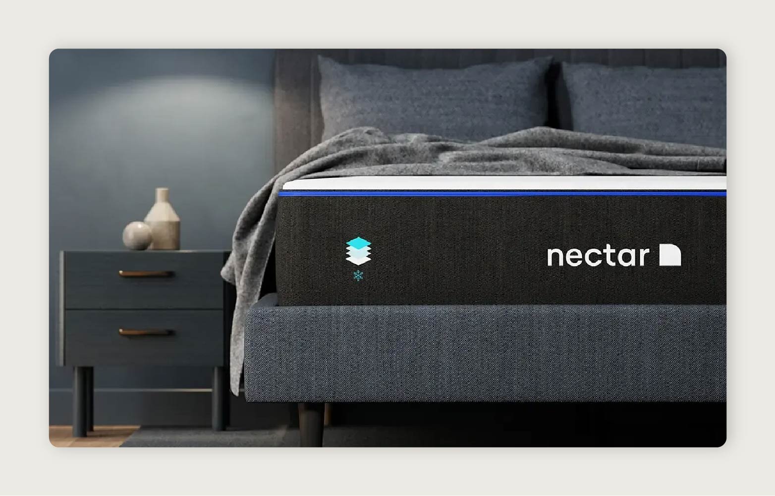 The Nectar Memory Foam Mattress shown in a dark gray room next to a bedside table. 