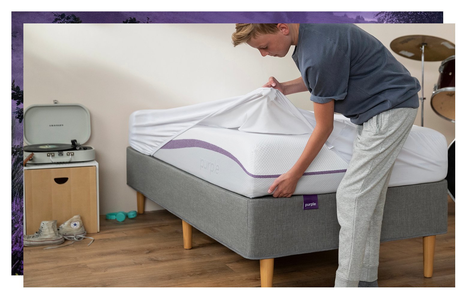 A teen boy puts a white sheet on a twin sized mattress.