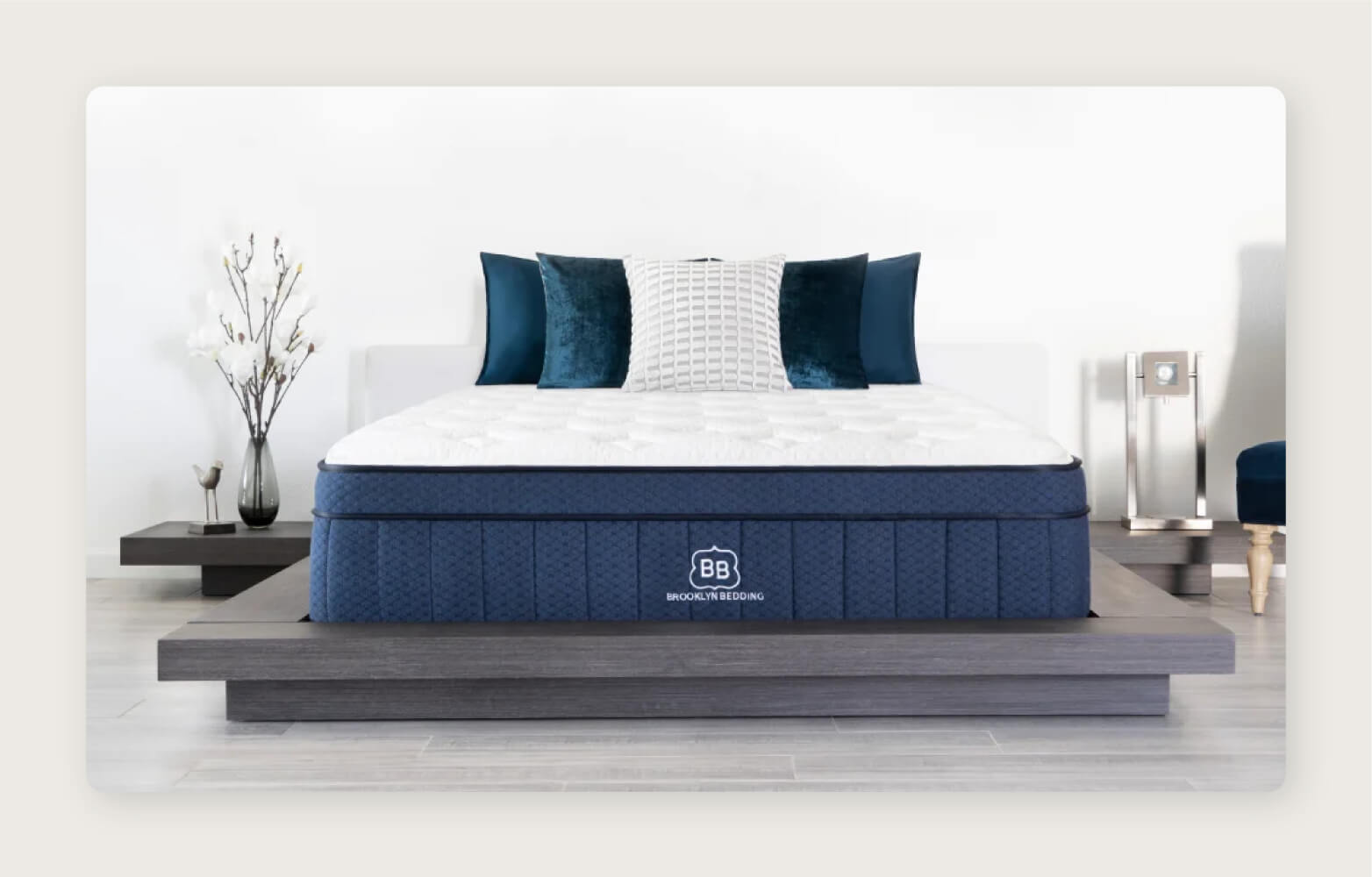 A blue Brooklyn Bedding Aurora Luxe mattress with throw pillows on a dark, low platform frame.