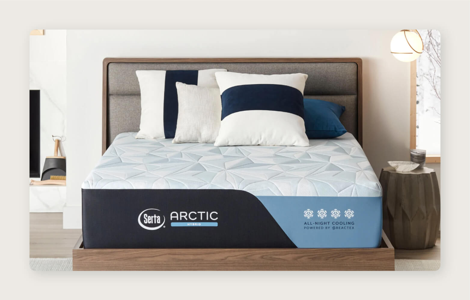 A Serta Arctic Hybrid Mattress with pillows on a wood bed frame in a bright white bedroom with wood accents.