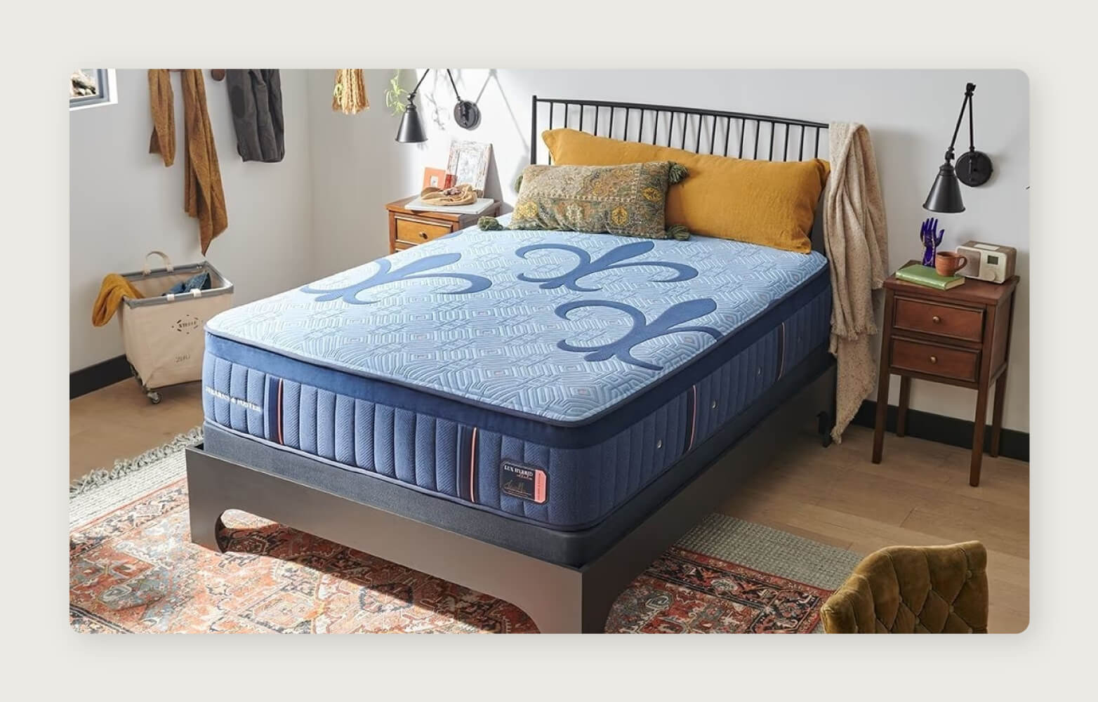 A blue Stearns & Foster Lux Hybrid mattress with pillows on a dark wood mid-century modern bed frame over a Persian-style rug.