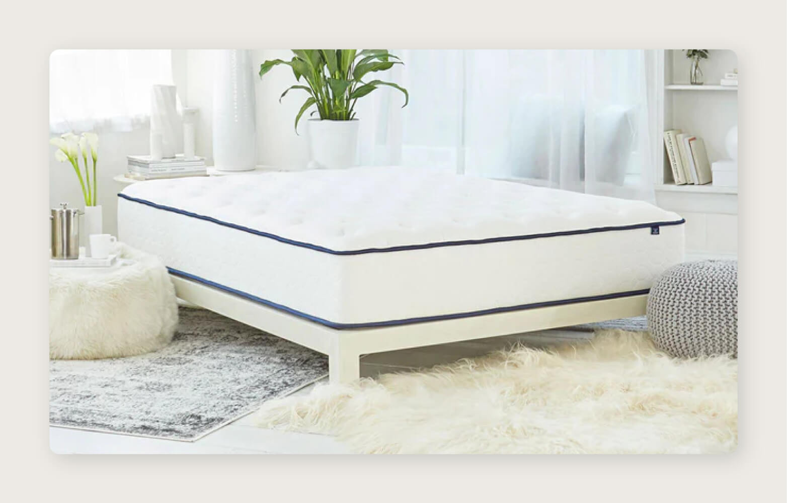 A WinkBeds GravityLux mattress sits on a white platform bed frame in a bright airy bedroom.
