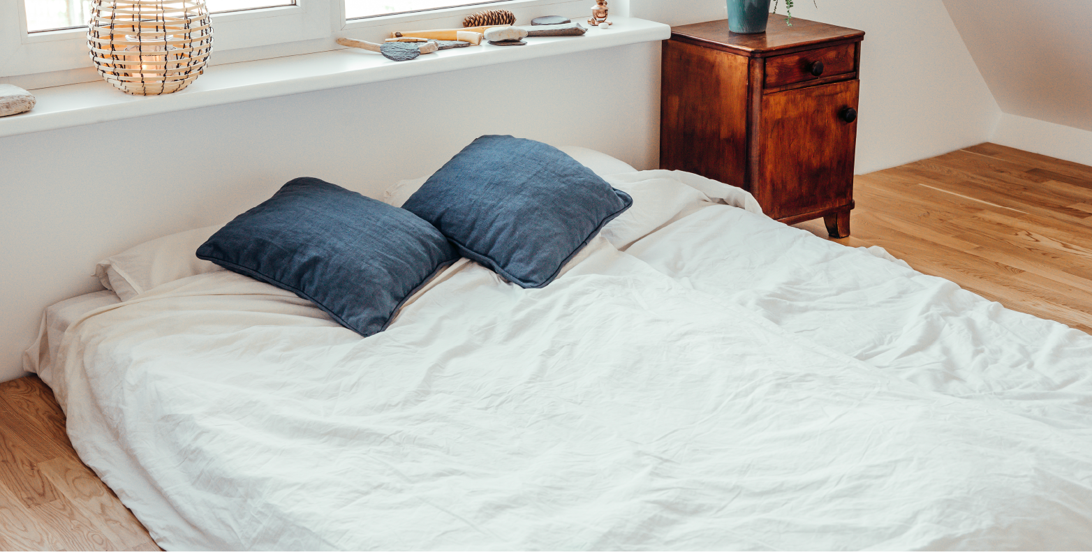 White mattress on the floor with two blue pillows.