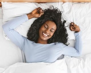 A smiling woman lying on her back in bed.