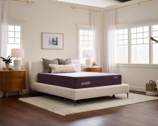 A queen Purple mattress on a cream bed frame in a bright airy bedroom.