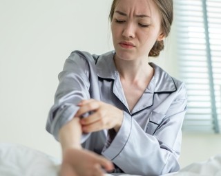 A person itching their arm while sitting in bed.