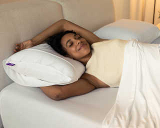 A woman stretching on a mattress and Purple Harmony pillow.