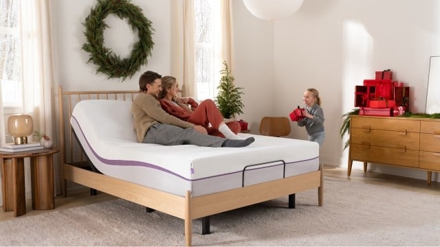 Man and woman sitting on mattress with child holding a red gift box