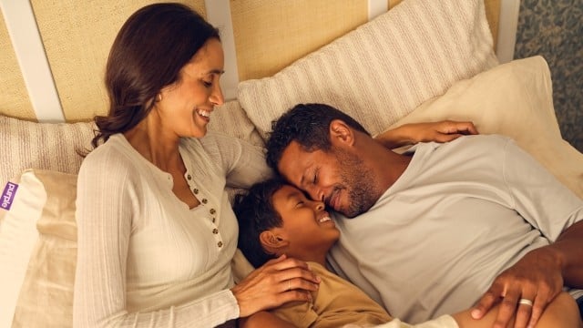 Woman, man and young boy smiling on bed