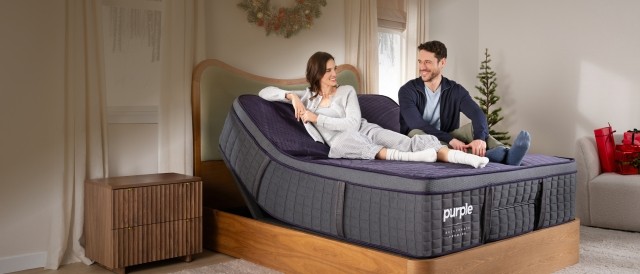Happy couple sitting on mattress with holiday wreath above headboard