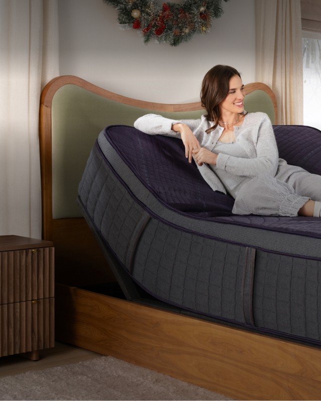 Happy woman sitting on mattress with holiday wreath above headboard