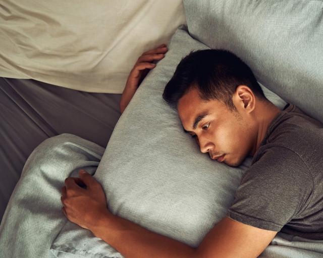 A man appears stressed while hugging and laying his head on a pillow.