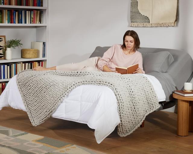 A woman reading a book while relaxing on an adjustable bed. 