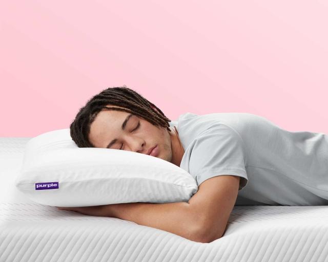 A man wearing comfy sweats sleeps on his stomach on top of an unmade Purple mattress using the Purple Harmony Pillow.