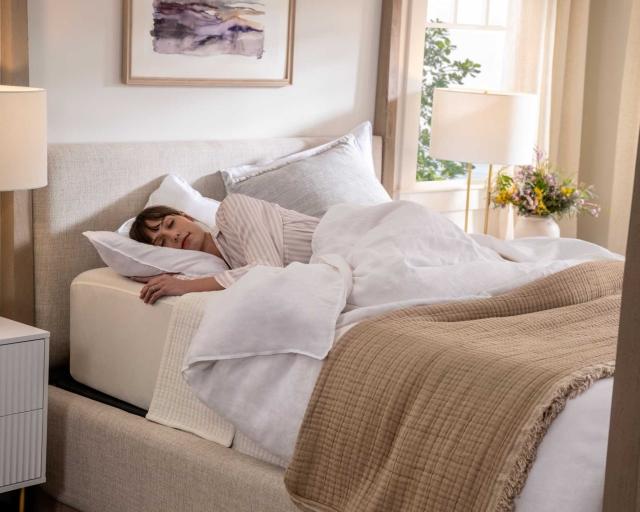 A woman sleeping on her side in a brightly lit room on a cozy bed