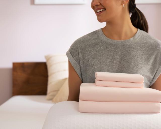 a woman carries a stack of pink pillows 