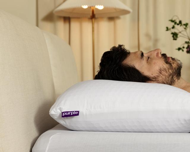 A man sleeps on his back on a Purple pillow