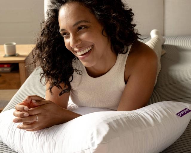 A happy woman rests on the Purple Harmony pillow.