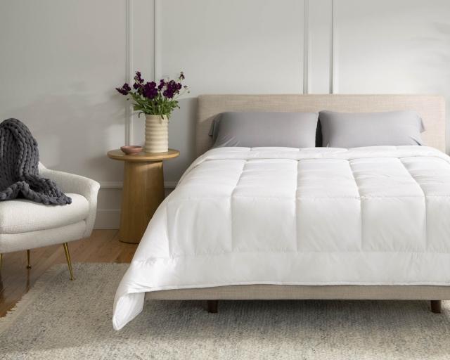 A queen bed with white and grey bedding between two wooden nightstands.