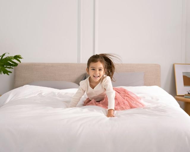 A young girl sits on a bed with a white duvet.
