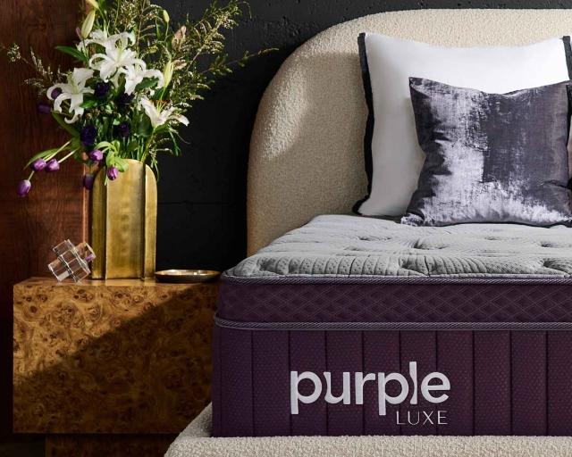 Purple RejuvenatePlus™ Mattress on a sherpa bed frame next to a nightstand with a large bouquet.