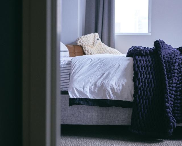 A navy blue knitted weighted blanket at the end of a bed. 