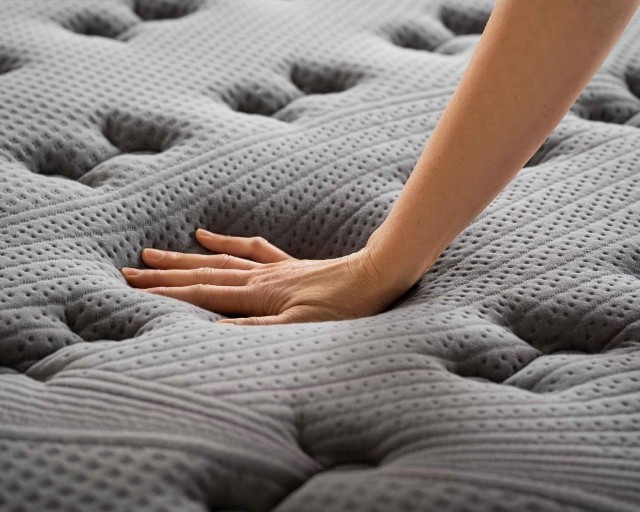 Hand pushing down on a grey Purple Rejuvenate latex mattress.