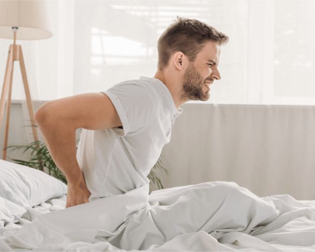 A man wakes up with a sore back after sleeping on a bad mattress.