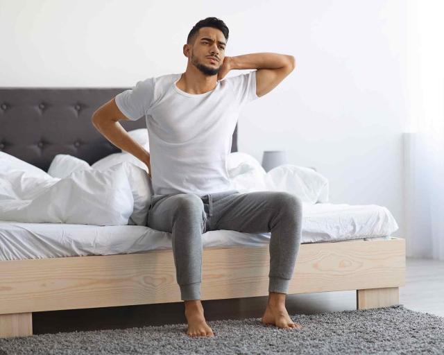 Man sitting on foot of bed in pain after sleeping on a sagging mattress
