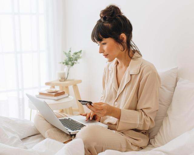 A woman in bed using a laptop to buy a mattress online.