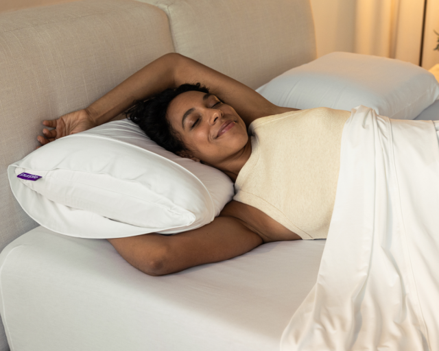 A woman stretching on a mattress and Purple Harmony pillow.