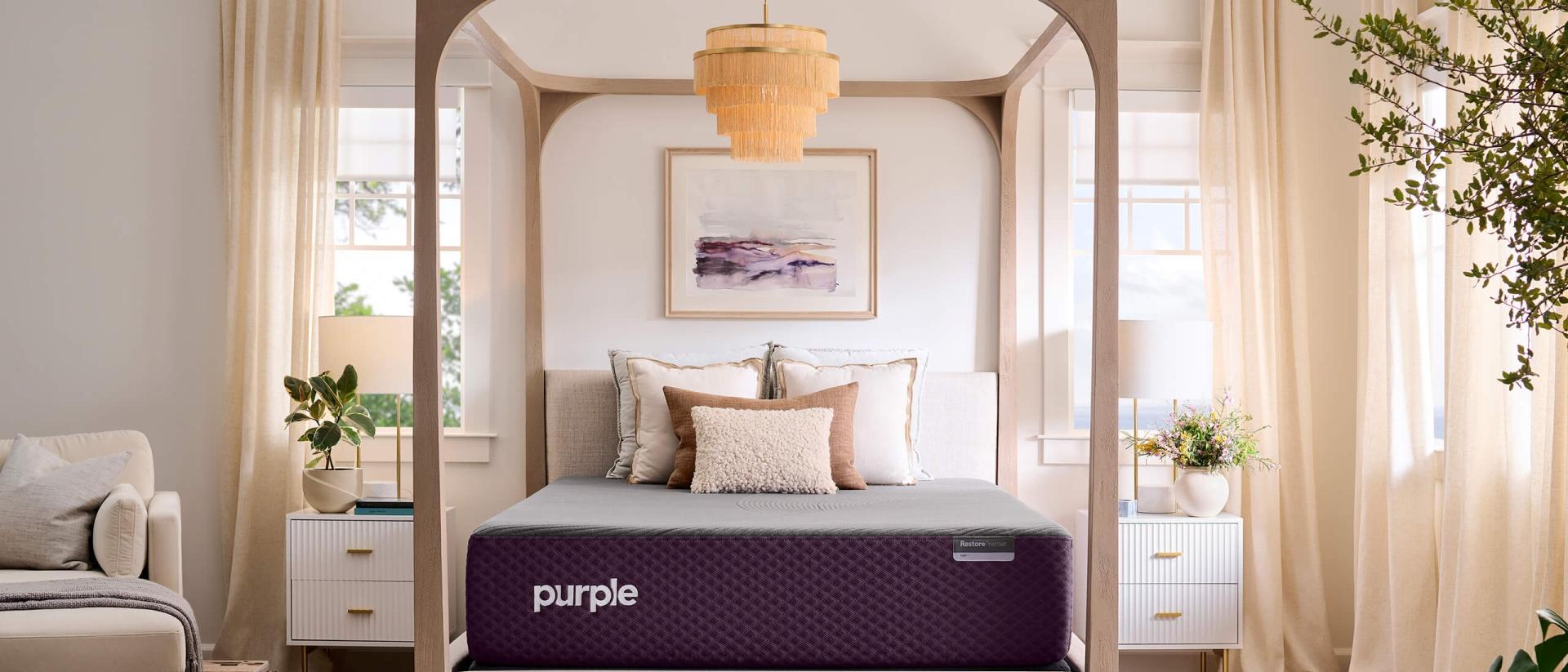 A Purple RestorePremier Hybrid mattress sits on a four poster canopy bed frame in a bedroom with ivory accents.