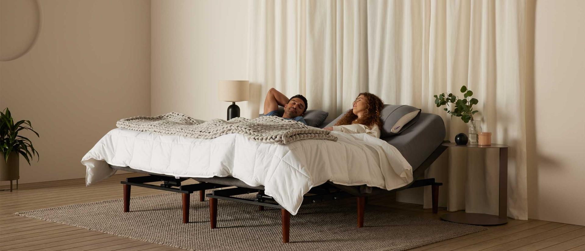 A couple sleeping together in a bed in a large room with white curtains. 