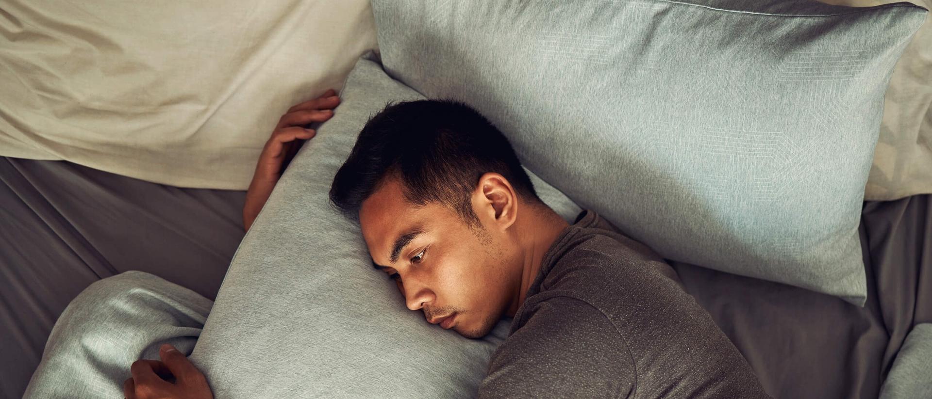 A man appears stressed while hugging and laying his head on a pillow.