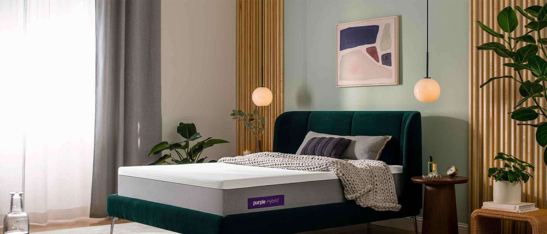 A Purple Hybrid mattress on a velvet green bed frame in a modern bedroom.