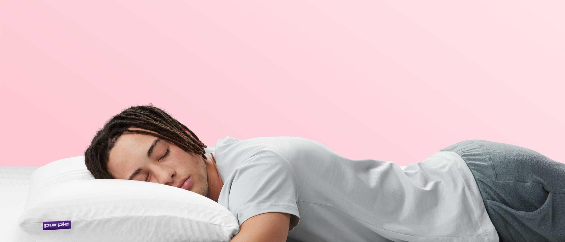 A man wearing comfy sweats sleeps on his stomach on top of an unmade Purple mattress using the Purple Harmony Pillow.