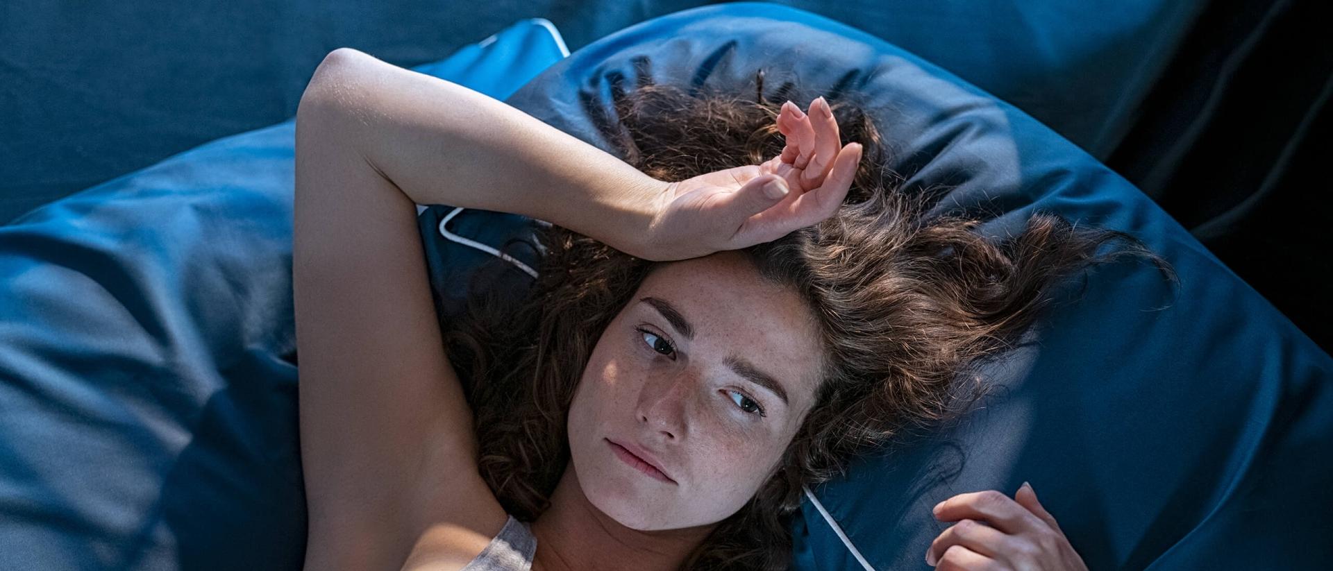 A woman lies awake on a blue bed due to hot sleep