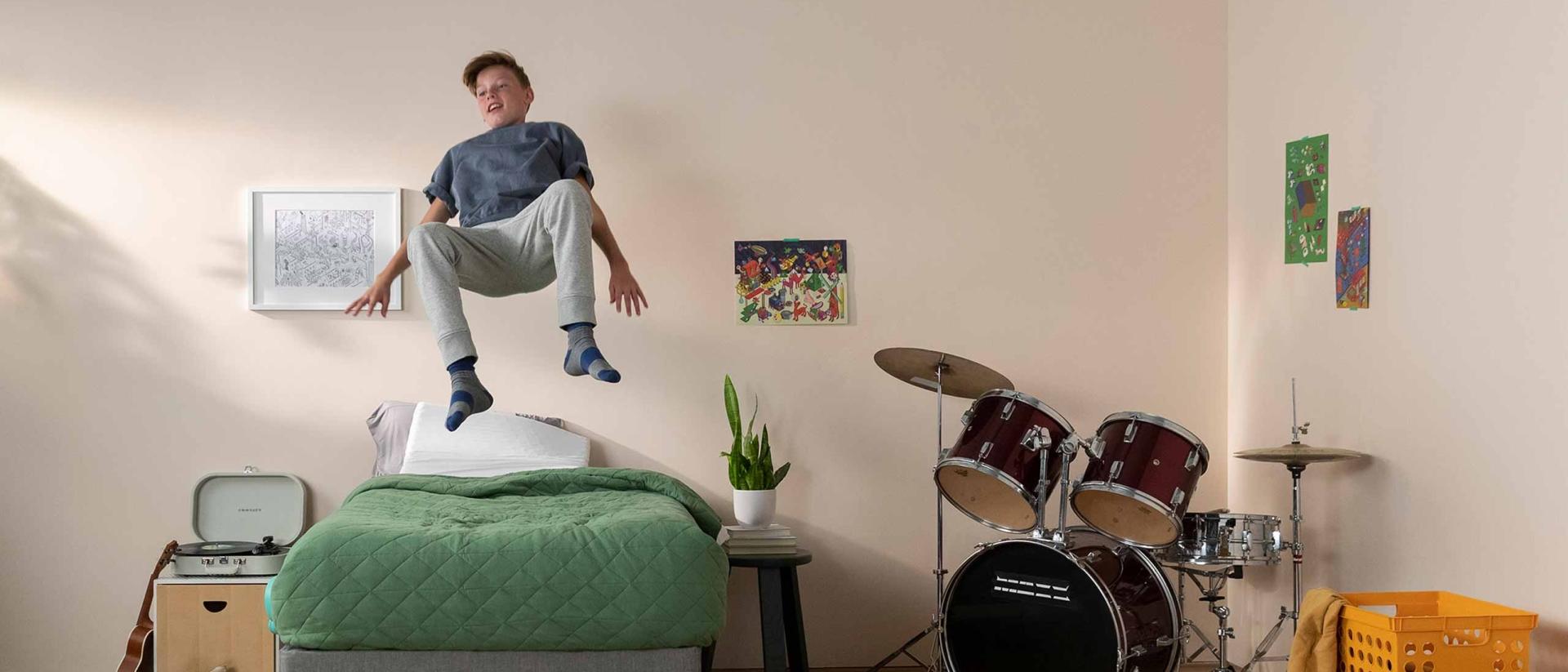 An exuberant child jumping on a twin size mattress in a bedroom.