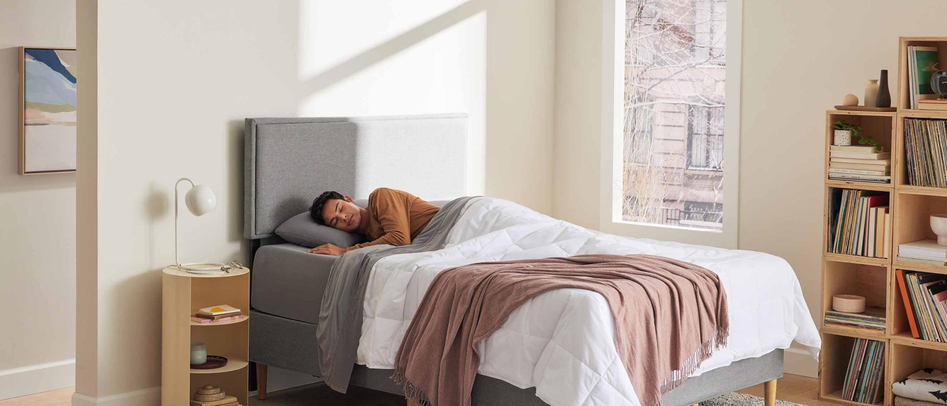 Man sleeping in a bed with a grey upholstered bed frame. 