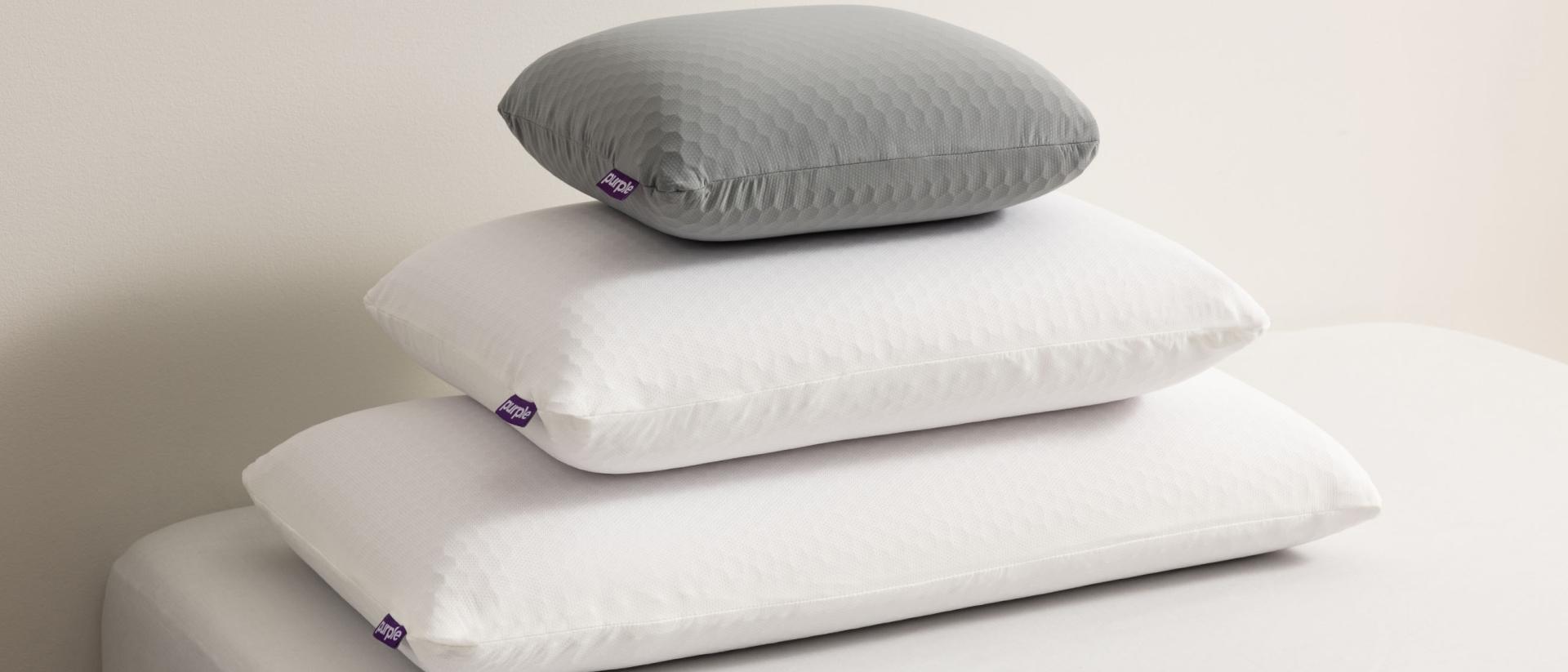 Three Purple pillows stacked on top of each other on a bed from largest to smallest 