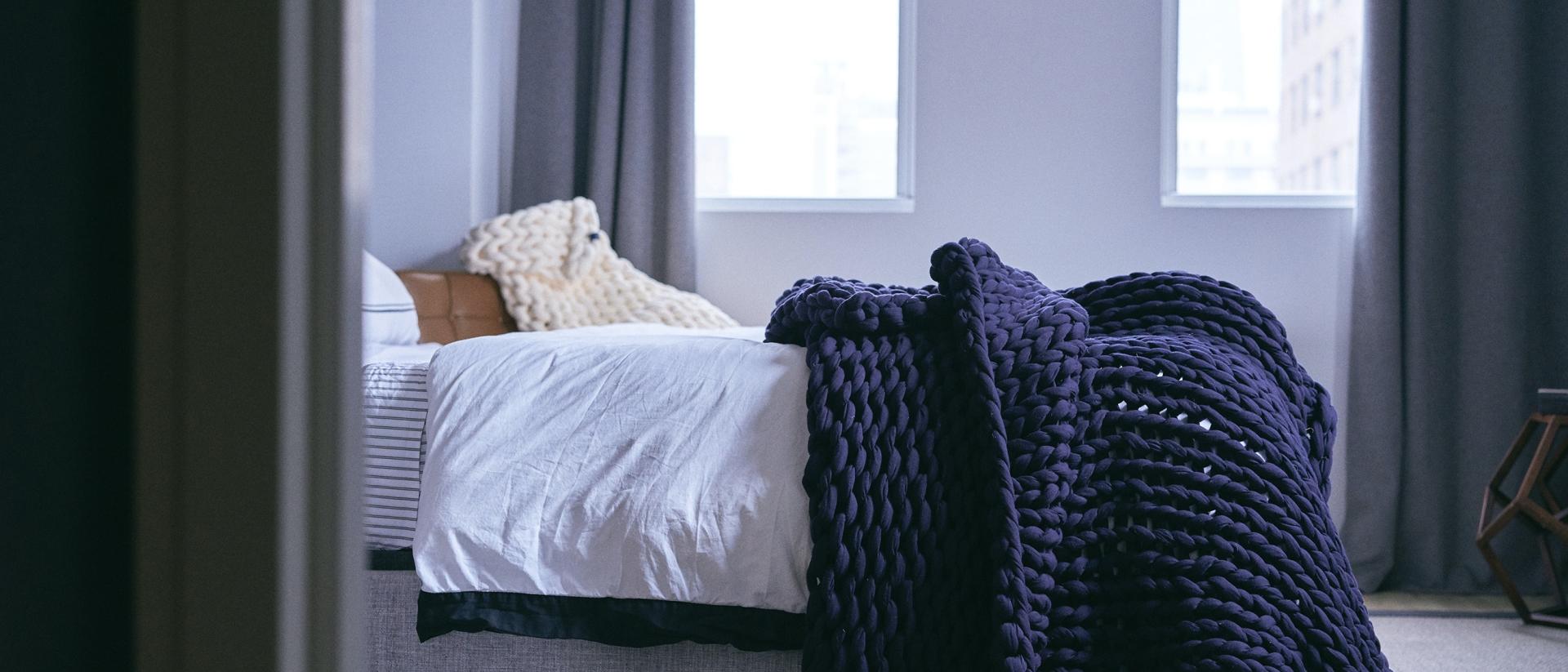 A navy blue knitted weighted blanket at the end of a bed. 