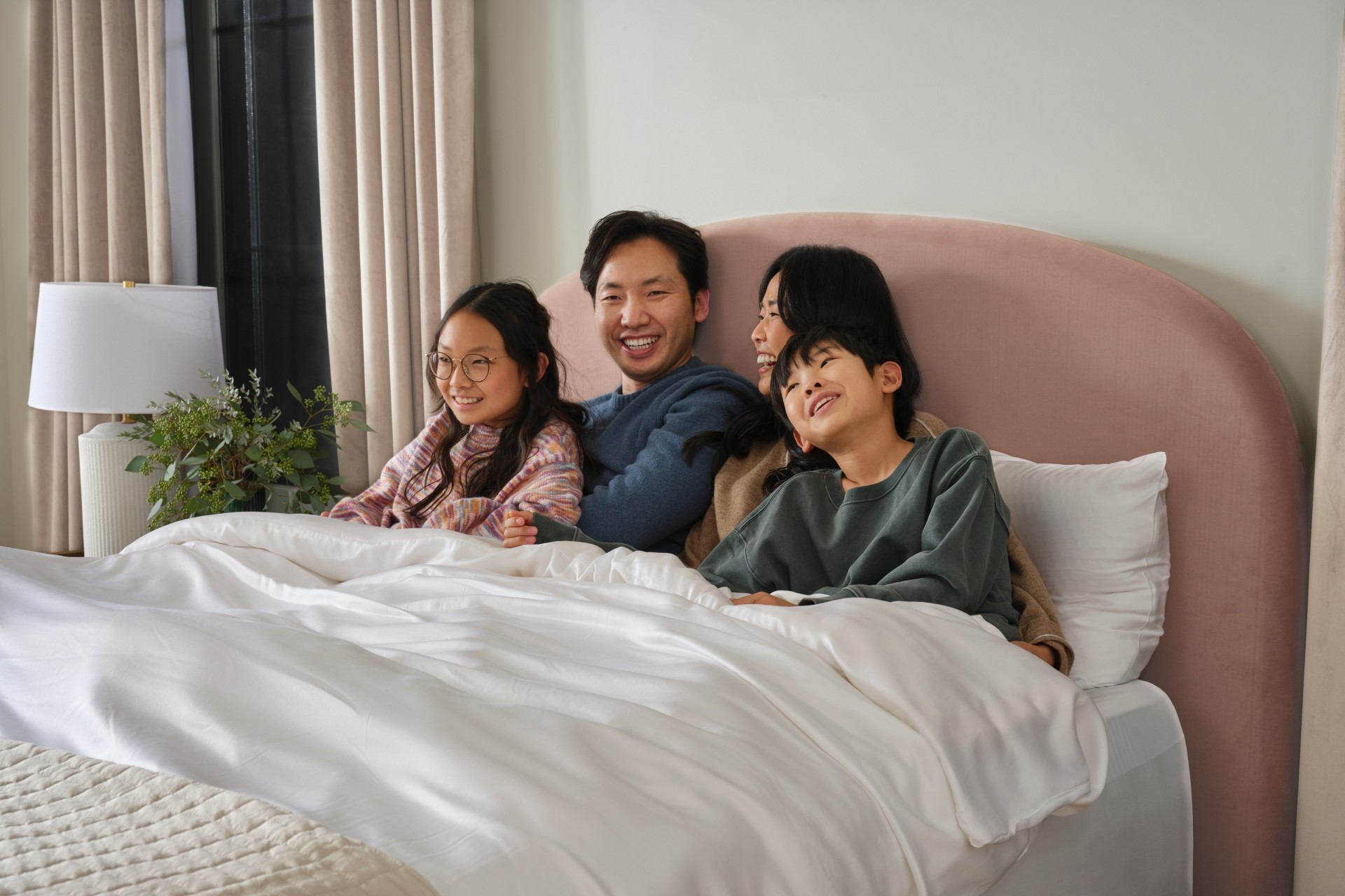 Family with woman, man and two children lying in bed under white duvet